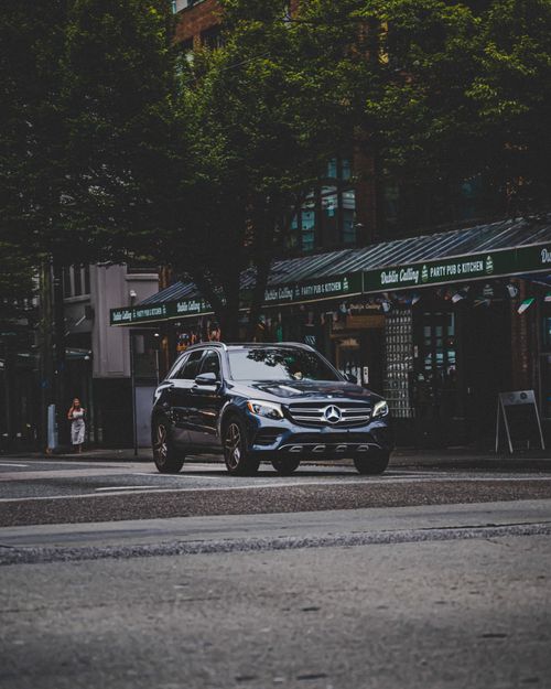 Free A Mercedes car drives through a rainy urban street, showcasing modern city life. Stock Photo