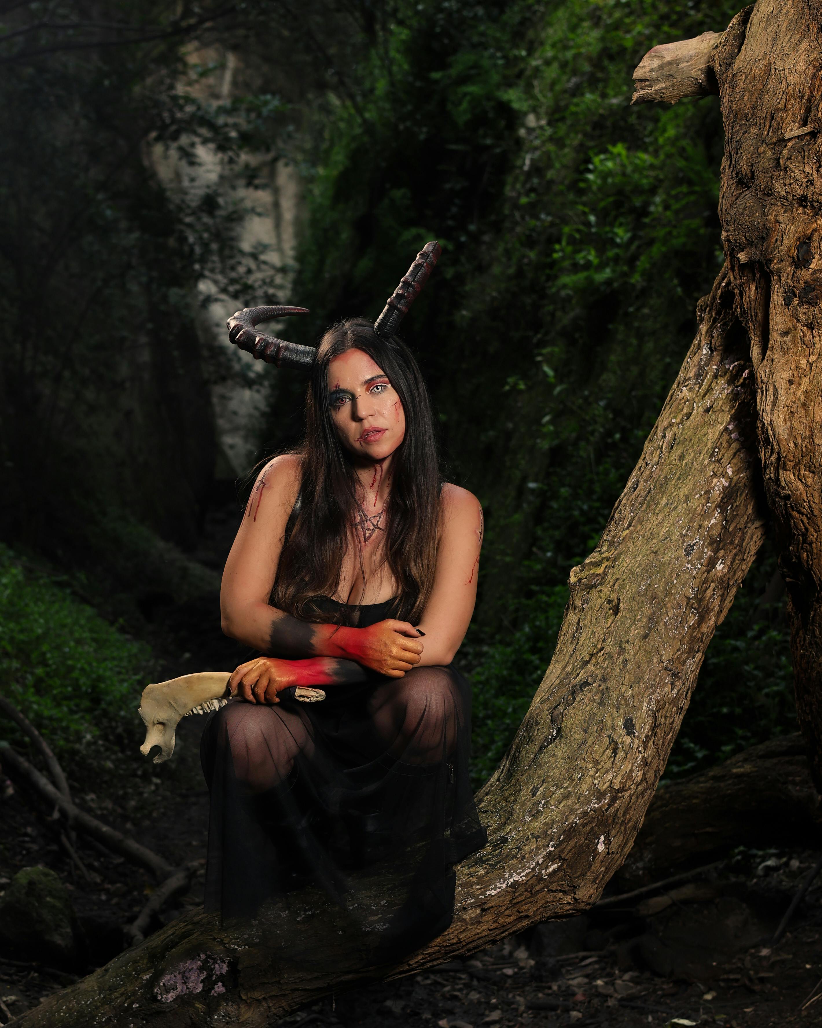 grátis Mulher Fantasiada De Diabo Segurando Mandíbula De Animal Agachada Em Um Galho Na Floresta Foto profissional