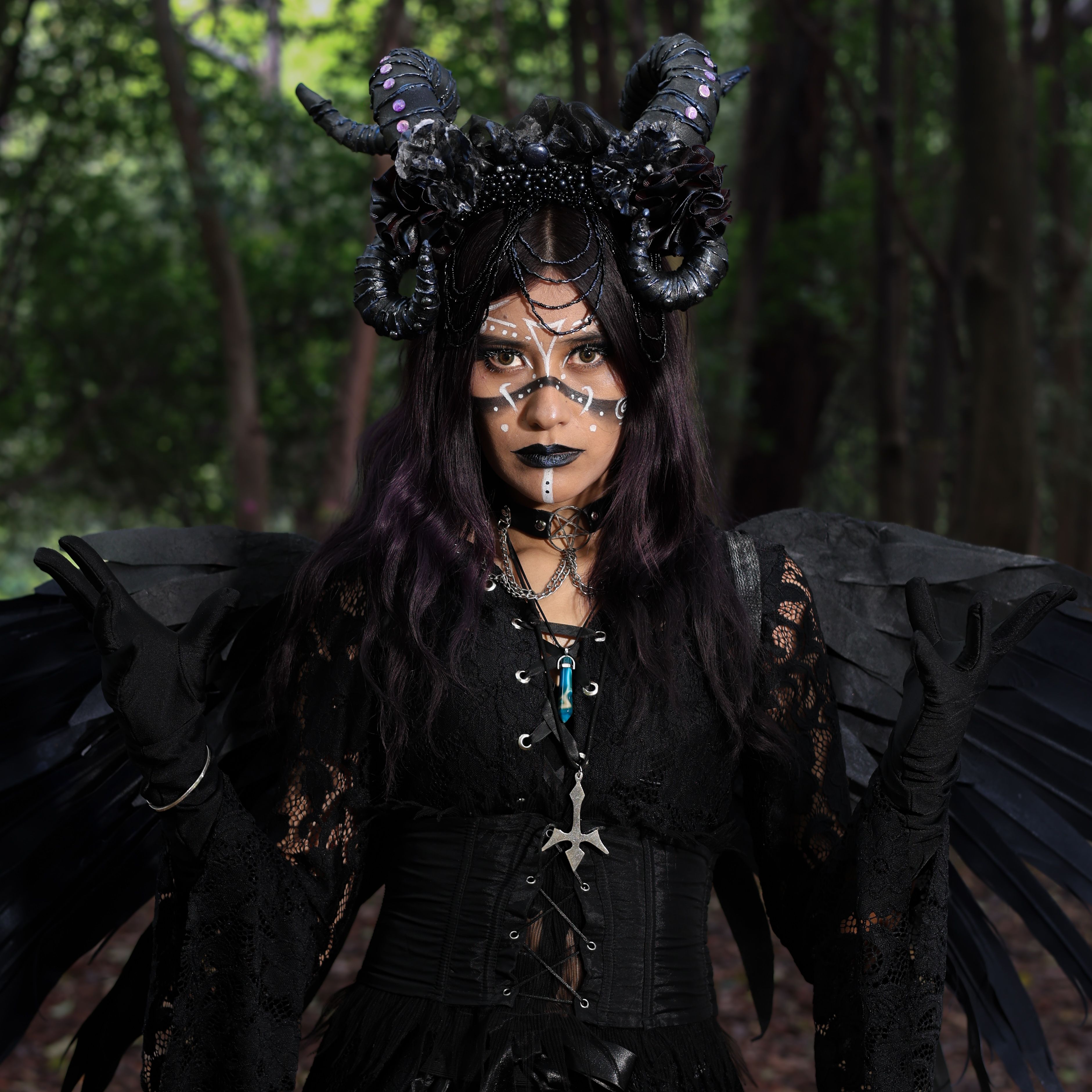 Portrait of a woman in forest wearing gothic costume with wings, horns, and stage makeup.