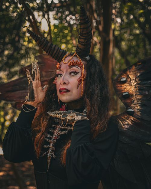 Free A woman in a fantastical costume with horns and wings in a forest setting, evoking a surreal and haunting atmosphere. Stock Photo