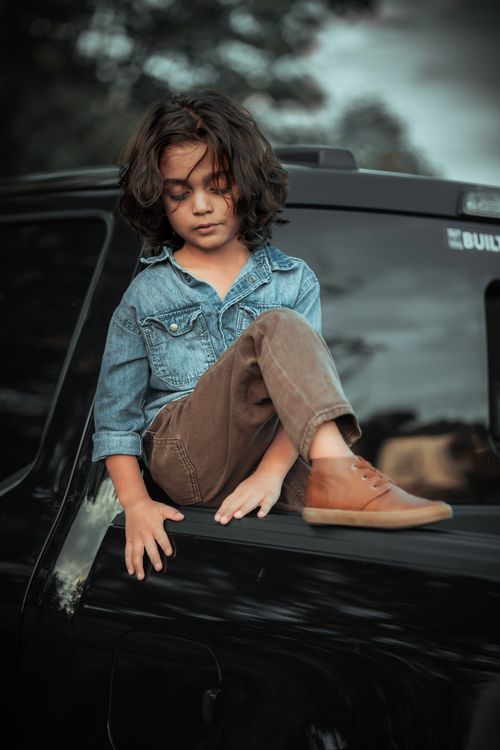 Free A child in jeans and brown pants sitting thoughtfully on a car, showcasing innocence. Stock Photo
