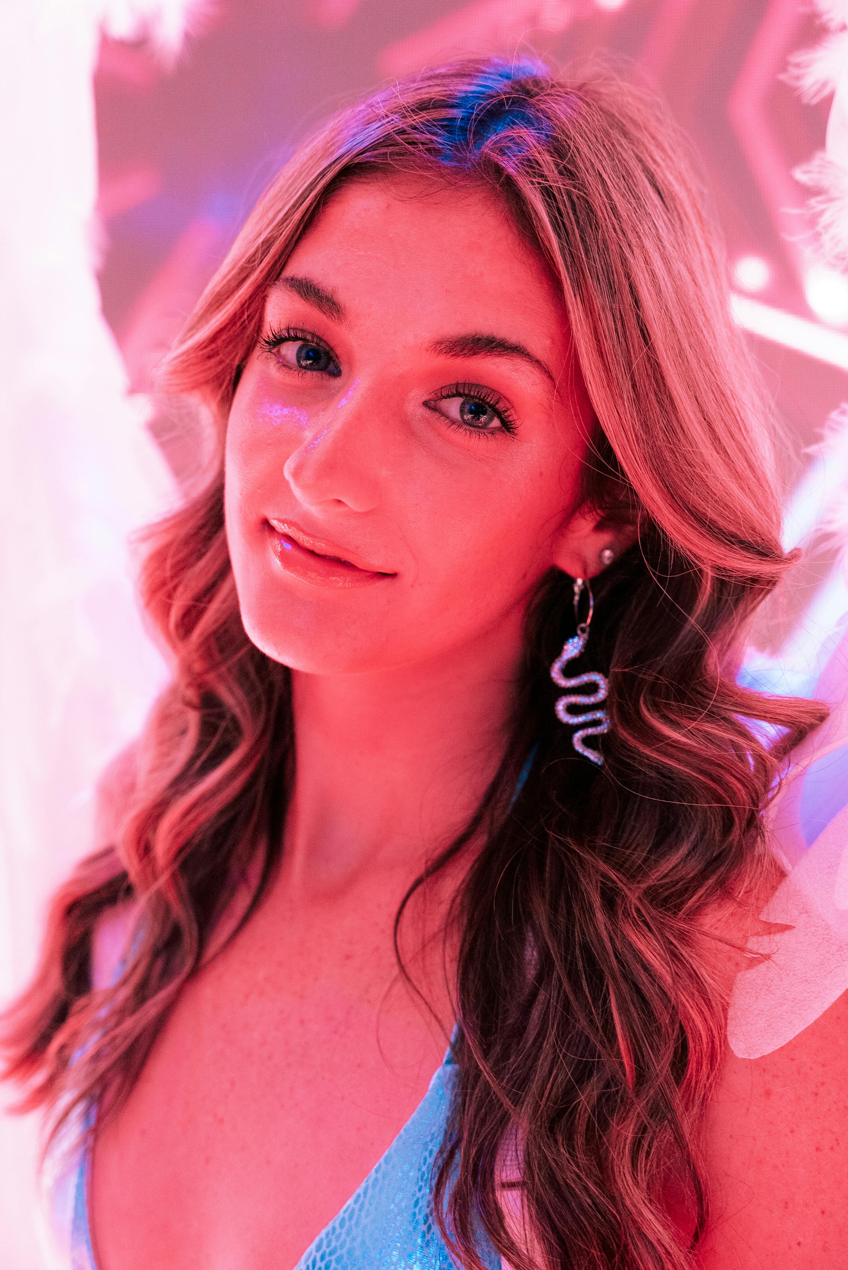 Portrait of a young woman with flowing hair and striking earrings against a colorful backdrop.