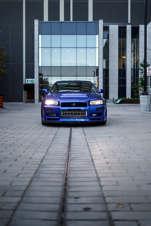 Free Blue Nissan GT-R sports car parked on urban street with modern architecture backdrop. Stock Photo