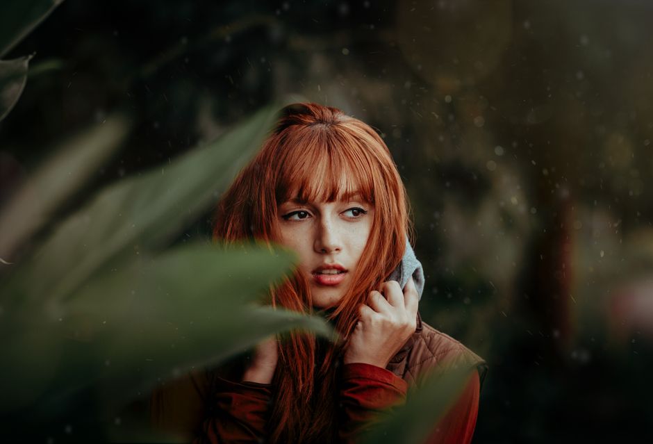 Captivating portrait of a red-haired woman in a forest setting, exuding beauty and mystery.