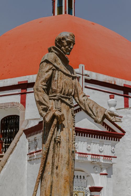 Free Rustic statue of a religious figure in front of a church with a red dome in Mexico's Amecameca. Stock Photo