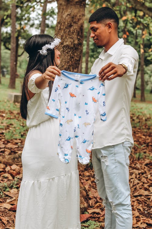 Pregnant Woman in White Dress and Man Holding Baby Clothes