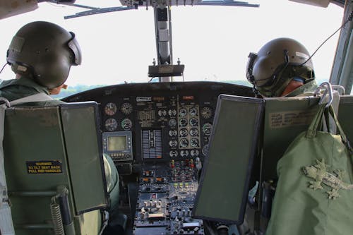 Back view anonymous male military pilots wearing khaki uniform in cockpit and helmets flying armed helicopter