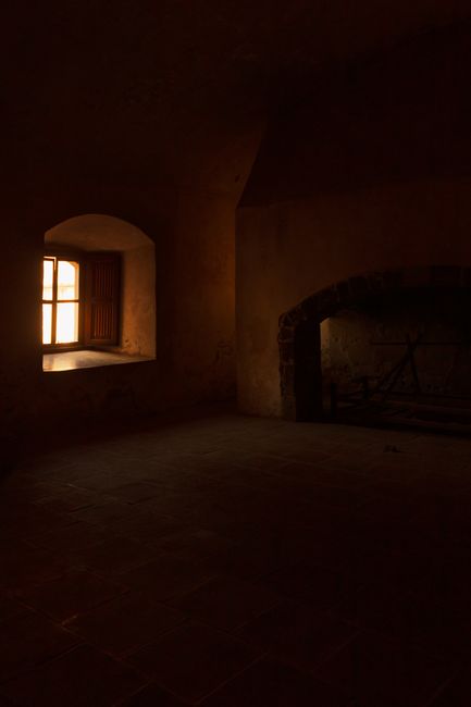 Moody interior of Saint Augustin Monastery in Acolman, showcasing a rustic dimly-lit room with window light.