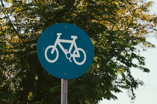 A clear bicycle lane sign against a backdrop of lush green trees, signifying a safe cycling path.