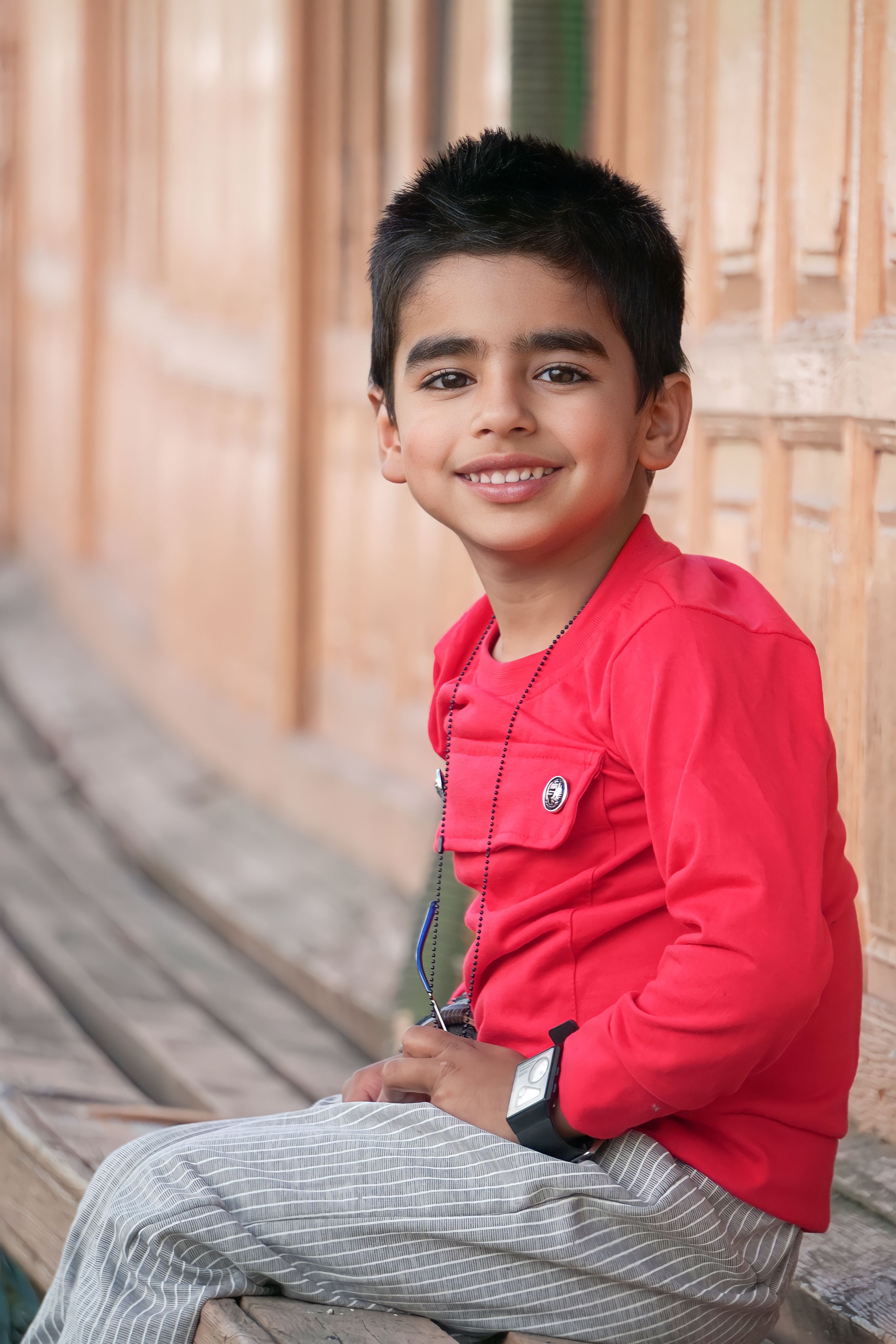 Happy young boy in red sweater smiling while sitting outdoors.