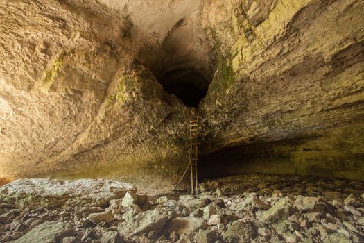 A rustic wooden ladder leading into the depths of a grand limestone cave, with rugged geological formations.