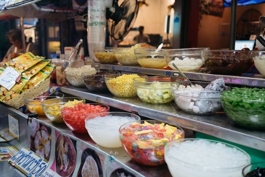 Colorful array of Thai desserts and ingredients at a bustling market stall, showcasing authentic culinary culture.