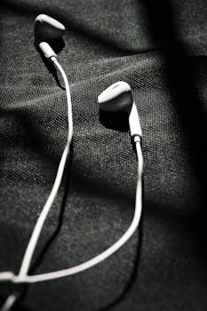 Black and white close-up of earphones resting on textured fabric surface.