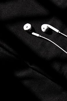 Black and white close-up of earphones on a textured fabric background with dramatic lighting.