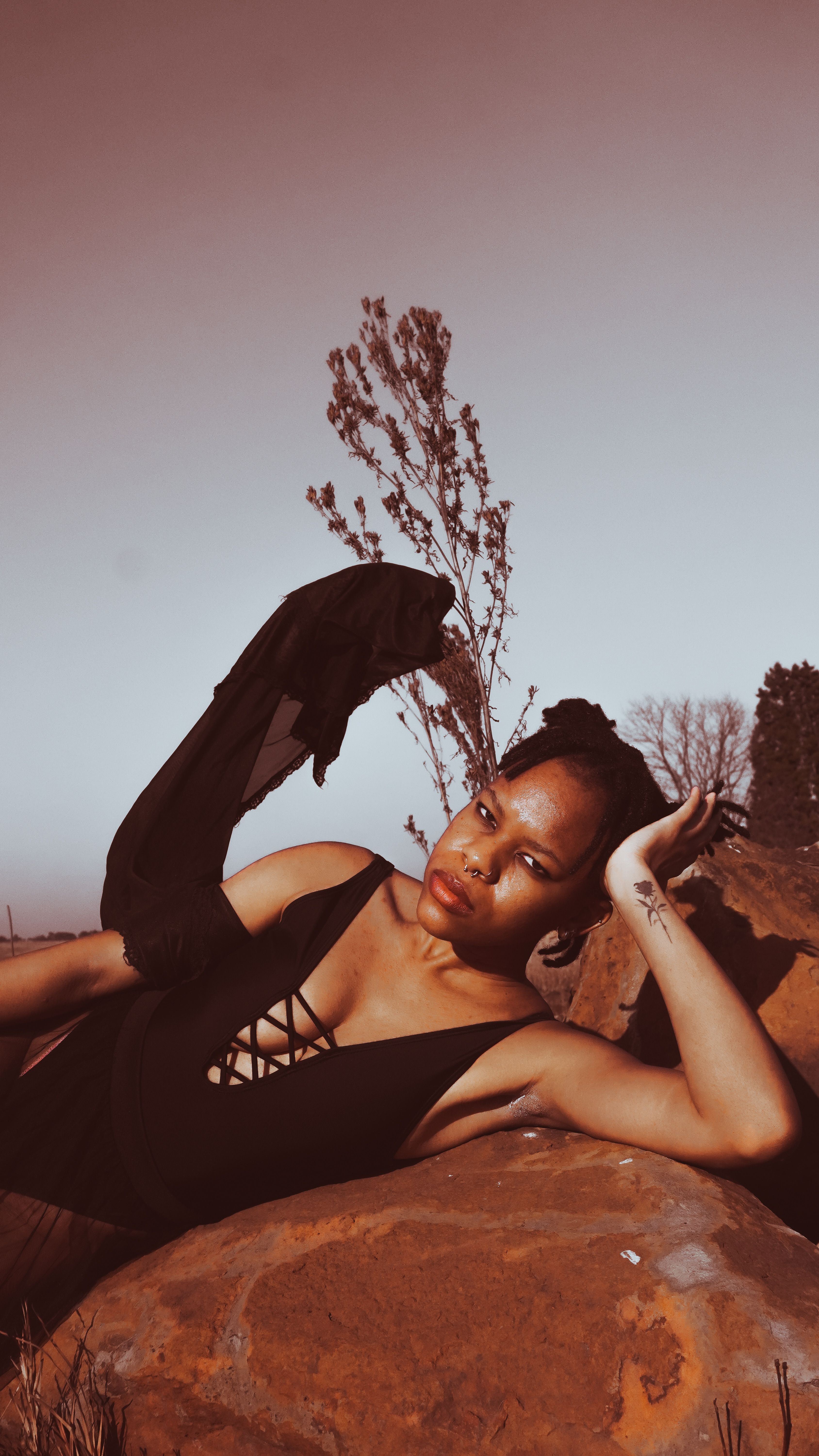 A stunning portrait of a woman in a black dress reclining outdoors, evoking a serene and elegant mood.