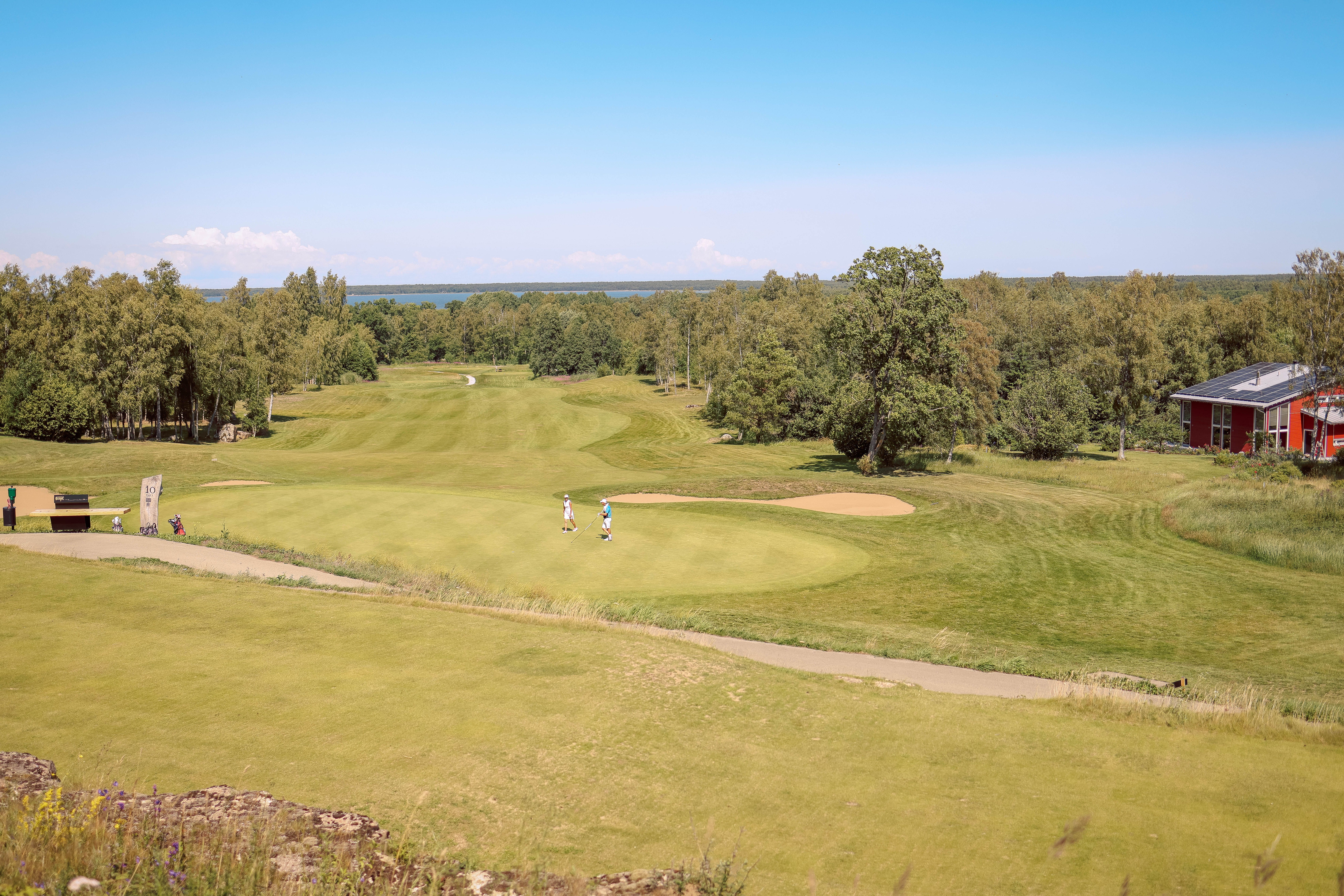 Aerial view of a picturesque golf course with players, surrounded by lush greenery.