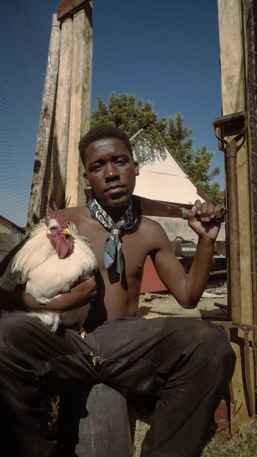A young man holding a chicken and a knife