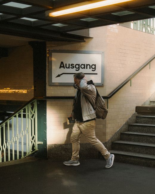 A man in casual attire walks up stairs at a Berlin station in a sunny urban setting.