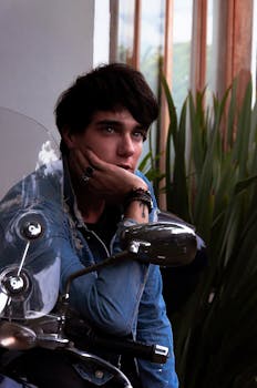 一位穿着牛仔夹克的英俊男子在室内骑着摩托车，若有所思地摆着姿势