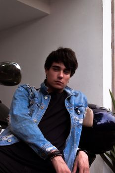一名时尚男子穿着牛仔夹克，在室内一辆摩托车旁自信地摆出姿势