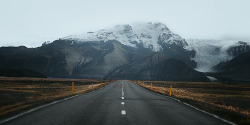 Free A serene road stretches towards majestic snowy mountains under a cloudy sky, showcasing breathtaking natural beauty. Stock Photo
