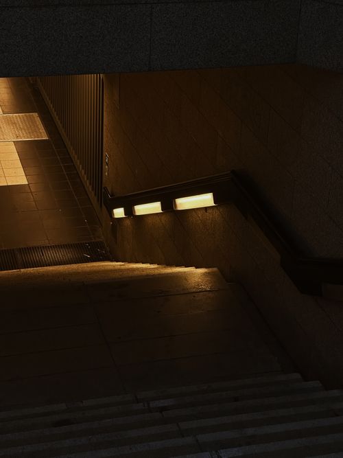 Free A moody view of an underground staircase illuminated by warm lights in an urban setting. Stock Photo