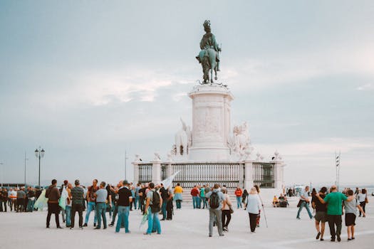 Tourists gather around the iconic statue in Lisbon, Portugal, enjoying a sunny day.