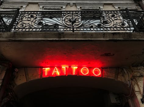 A vibrant red neon tattoo sign on an ornate building facade captures a moody urban atmosphere.