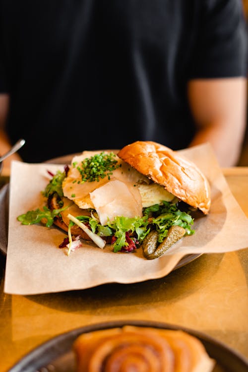 A sandwich on a plate with a person sitting at a table