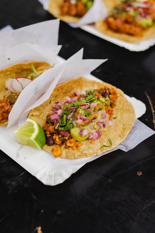 Tacos are served on paper plates with lime and onions