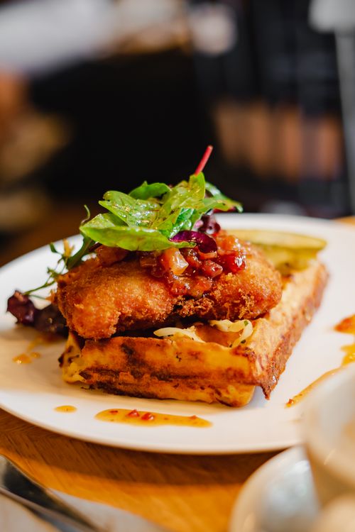 Free Close-up of a gourmet chicken and waffle dish topped with fresh greens on a white plate indoors. Stock Photo