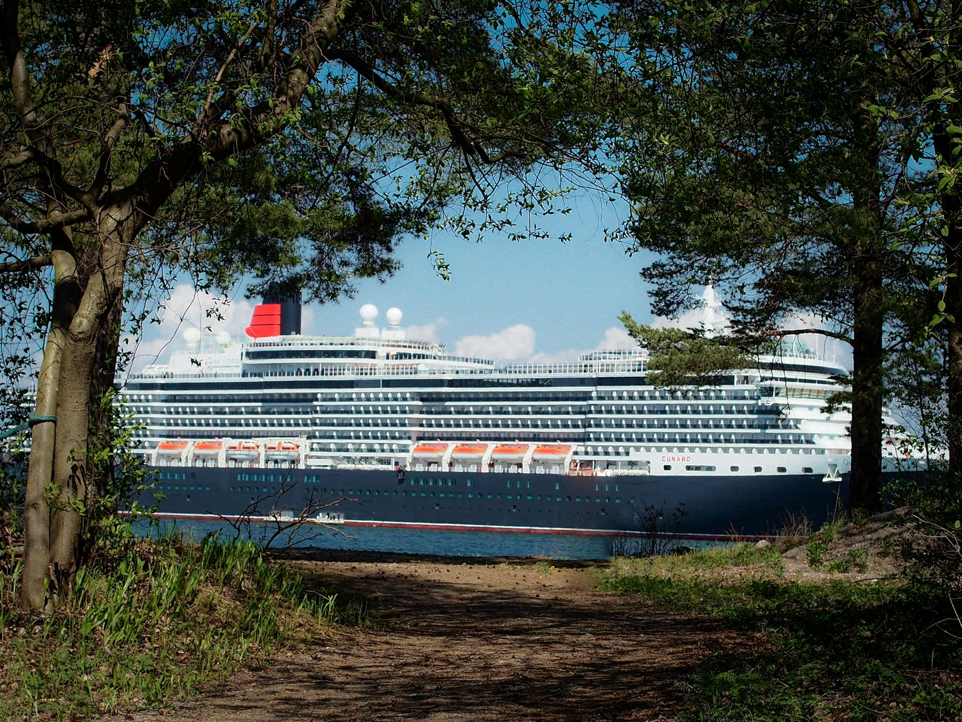 A cruise ship glides through Helsinki harbor, framed by lush trees.