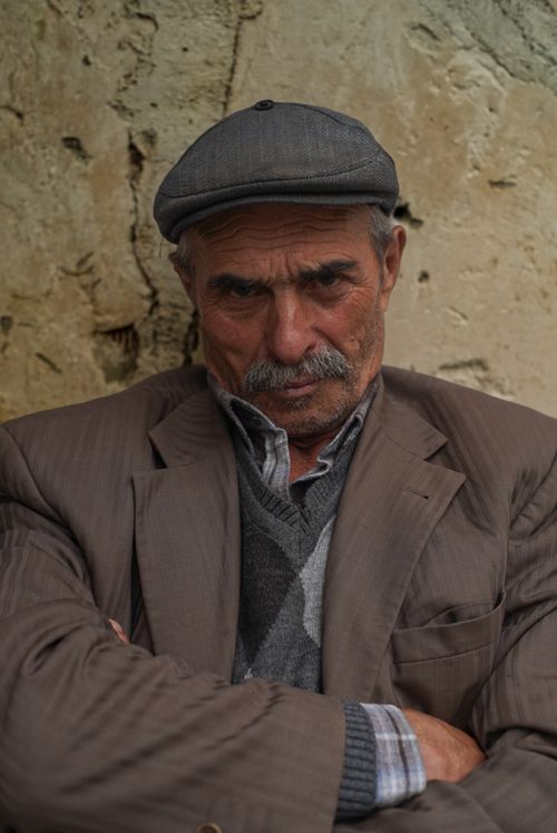 Free Thoughtful portrait of an elderly man wearing a cap and jacket against a rustic wall. Stock Photo