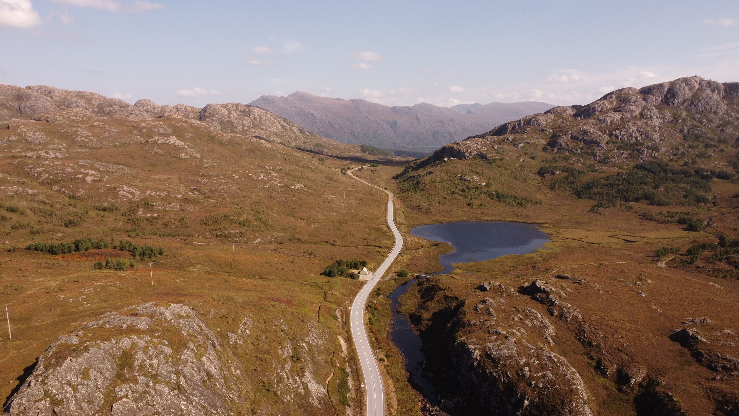 Aerial shot of a picturesque road weaving through the rocky landscapes of the Scottish Highlands