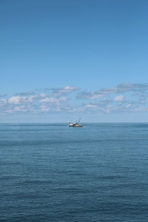 Free Calm open sea view with a solitary boat under a clear blue sky. Stock Photo