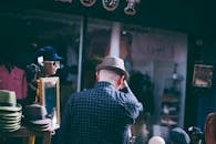 阳光明媚，一名男子在街头市场的摊位前浏览帽子