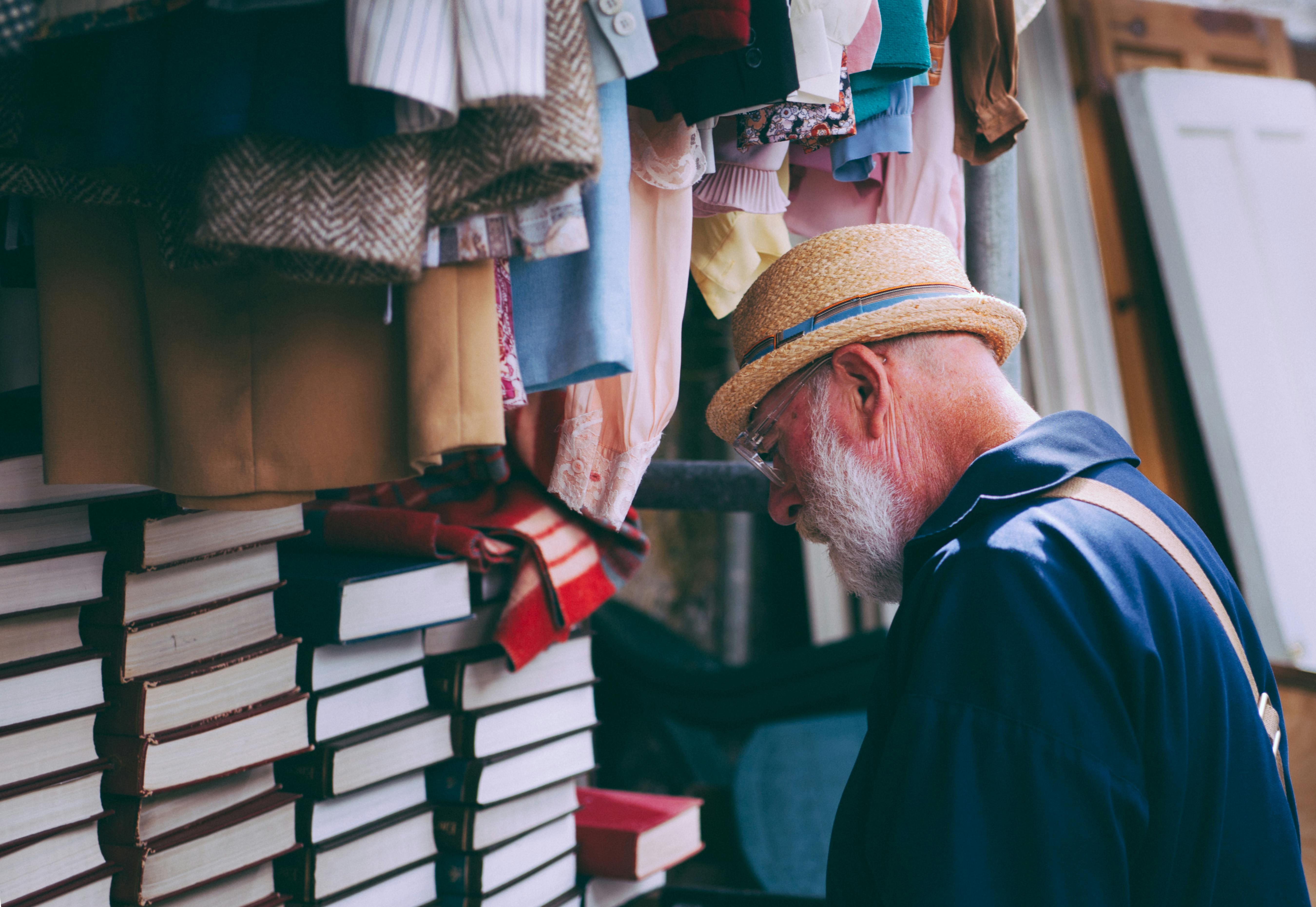 man in brown sun hat facing black covered piled books