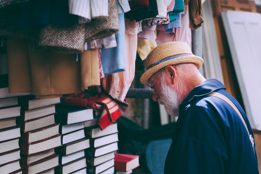 Senior man in a straw hat explores books and clothes at an outdoor market.