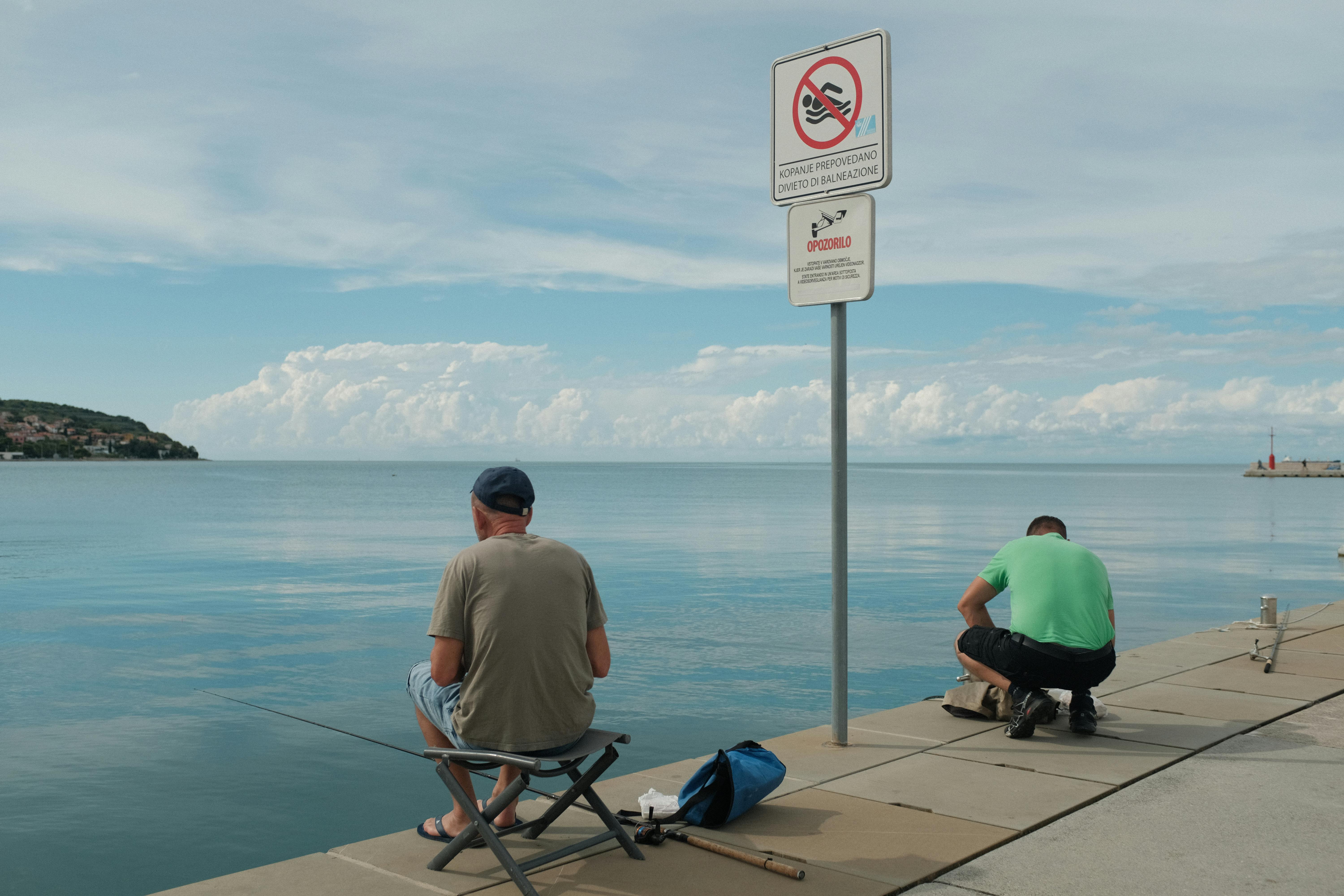 Two men enjoying fishing on a sunny day by the seafront in Koper, Slovenia.