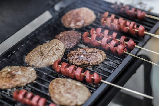 Close-up of grilled burgers and sausage skewers cooking on a barbecue grill outdoors.