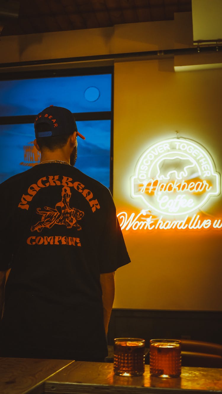 Man Standing By Bar Staring At Neon Sign