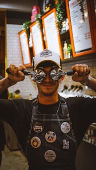 A cheerful barista uses espresso portafilters as eyeglasses in a lively café setting.