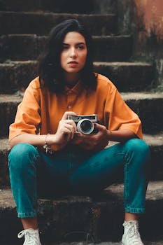 楼梯上，一位时髦的妇女拿着一台老式照相机，以坦率的姿势展示着休闲服