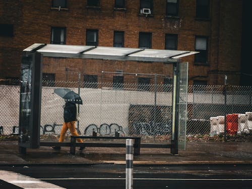Person with Umbrella Passing Empty Bus Stop in Industrial District 