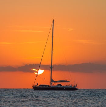 A sailboat glides across the sea against a vibrant sunset near the Balearic Islands.