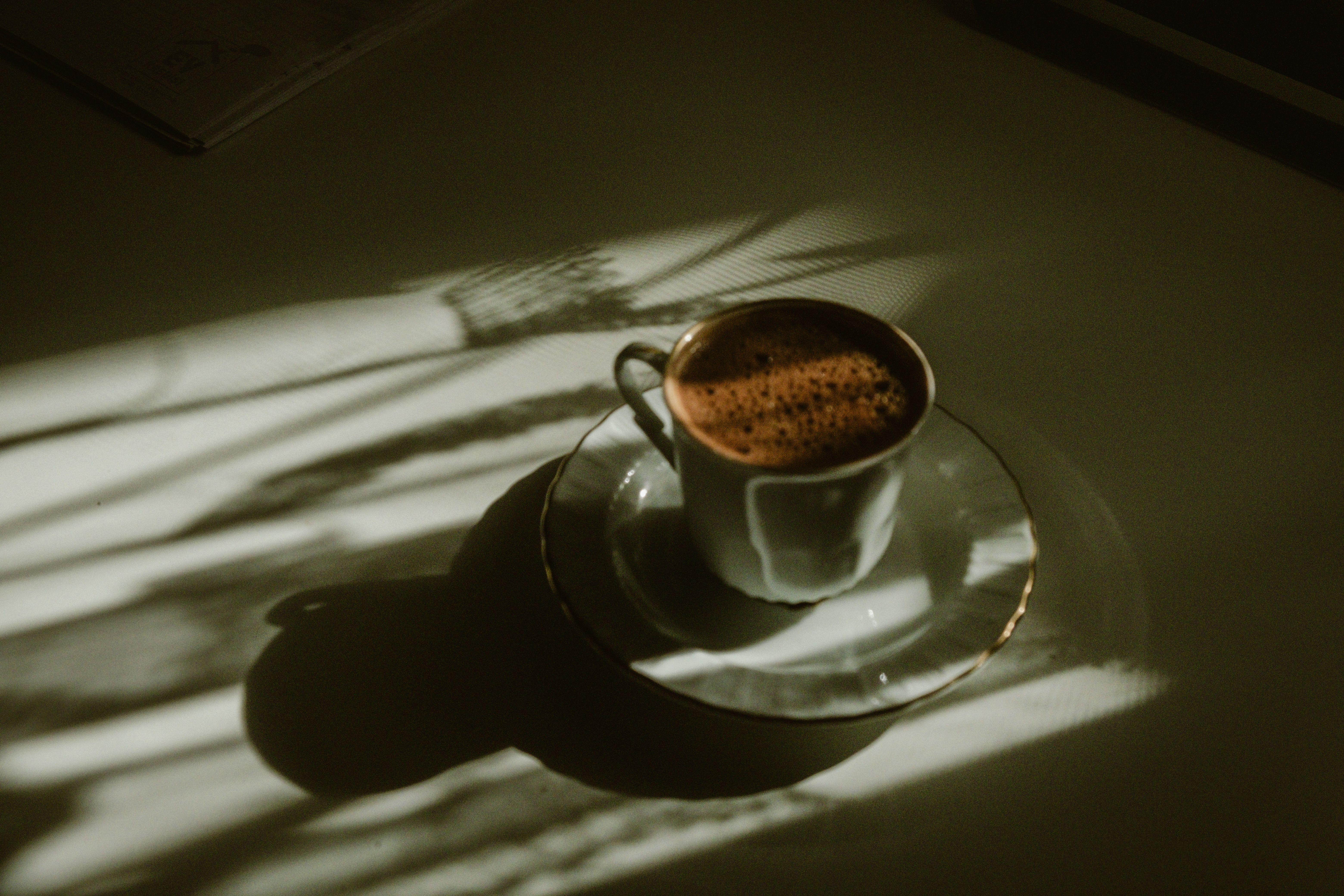 Artistic shot of a coffee cup on a table, illuminated by soft sun rays creating shadows — modafinil and coffee