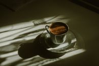 Artistic shot of a coffee cup on a table, illuminated by soft sun rays creating shadows.
