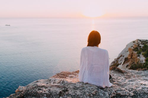 Free Woman Sitting on Gray Rock Near Body of Water Stock Photo