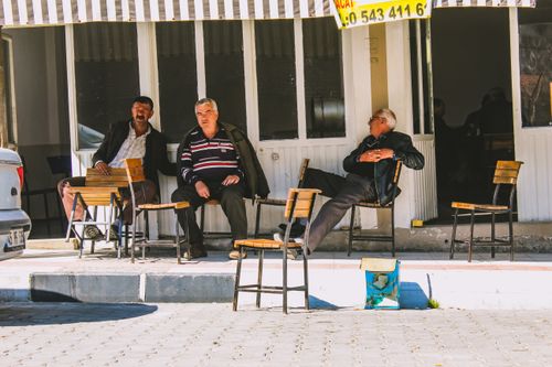 Free Three elderly men sitting and chatting outside an urban café on a sunny day. Stock Photo