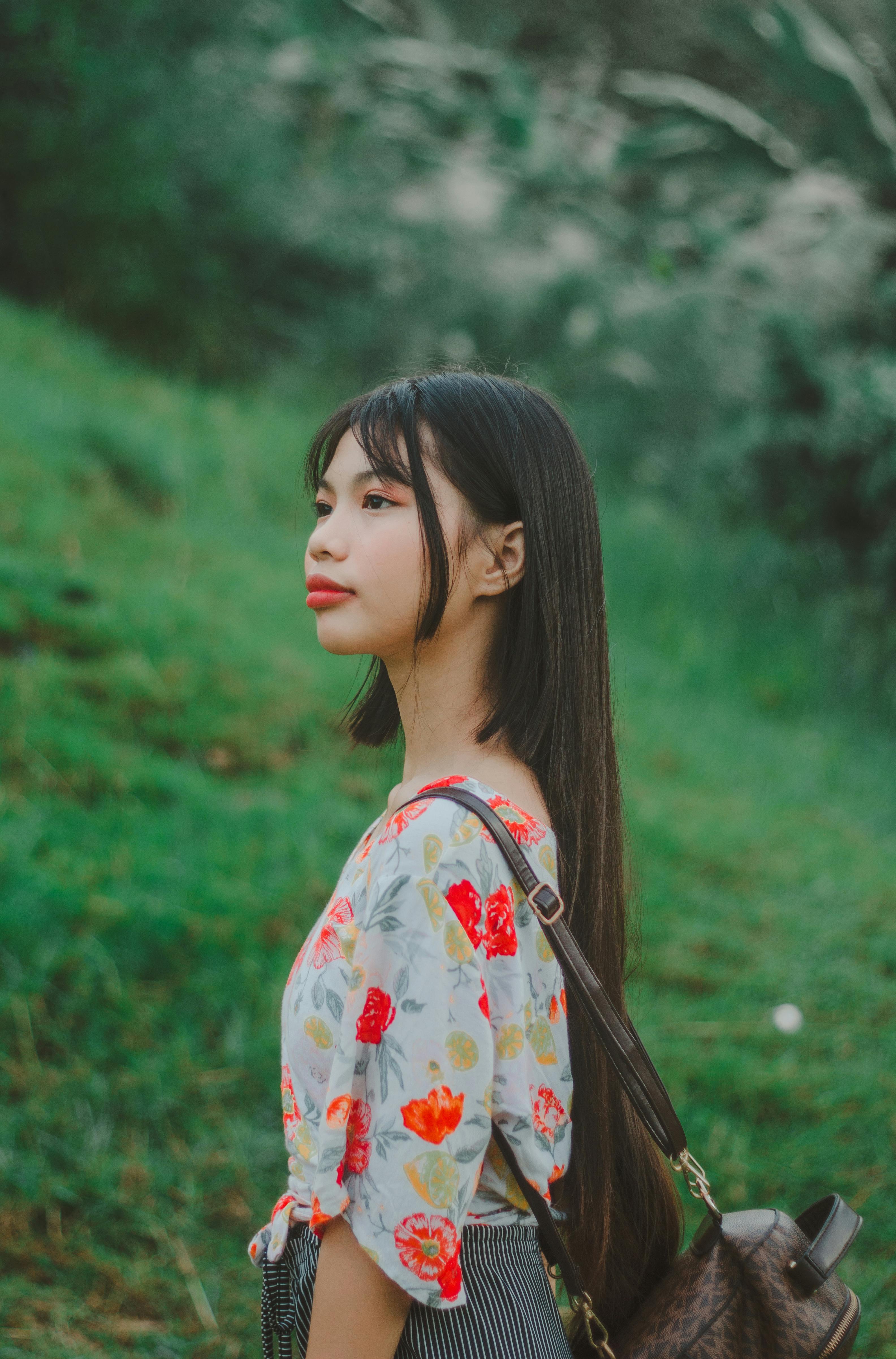 Profile portrait of a young woman in a floral top outdoors, evoking a serene and natural vibe.